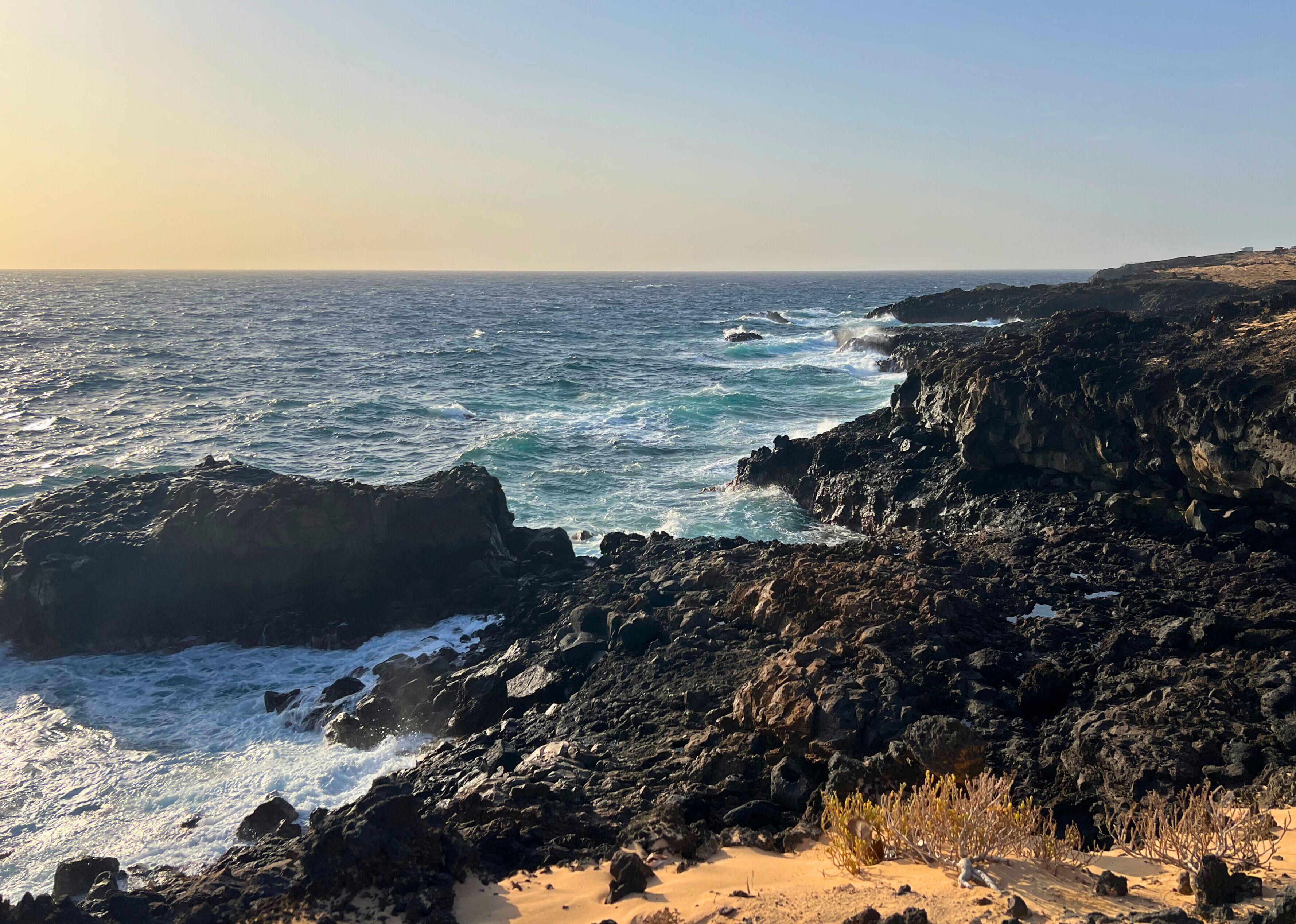 A rocky coastline with waves crashing against the rocks and a clear sky.