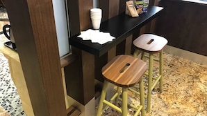A bar area with stools, a black countertop, and stacked white cups. - Nova Hotel Miri (Miri)