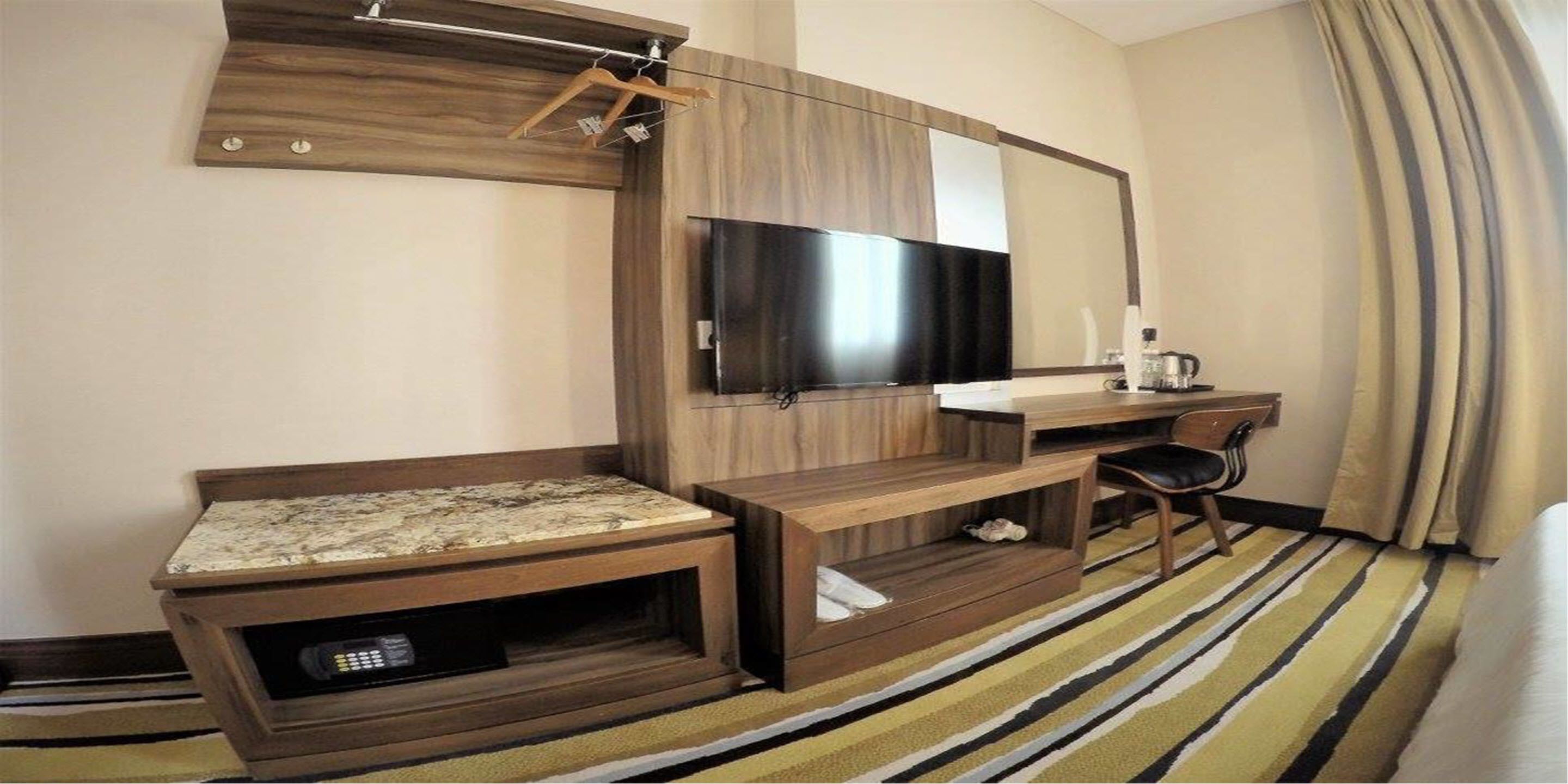 A hotel room with a wooden entertainment unit, a flat-screen TV, a desk, a chair, and a striped carpet.