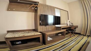 A hotel room with a wooden entertainment unit, a flat-screen TV, a desk, a chair, and a striped carpet.
