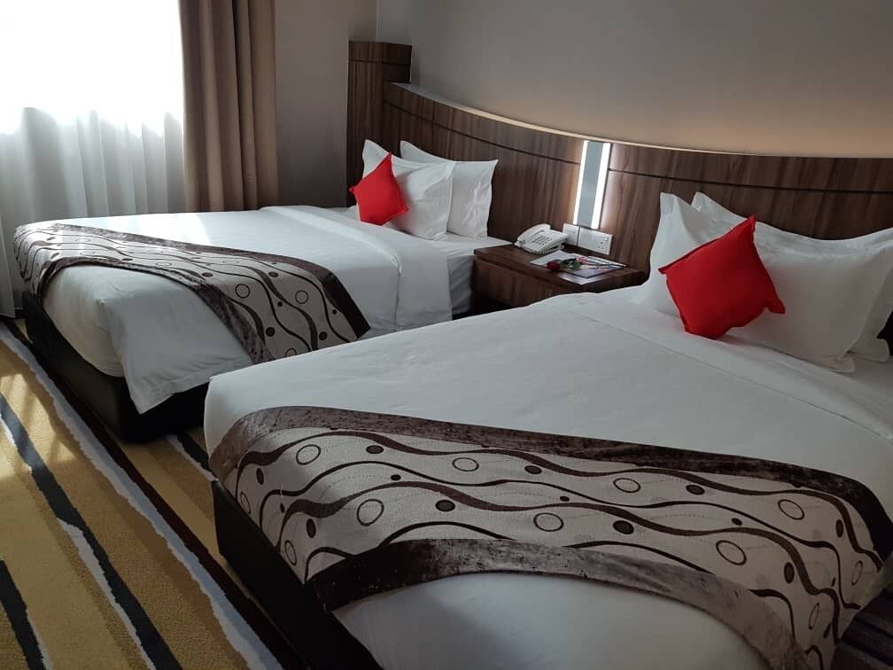Two double beds with white linens and red pillows, a bedside table with a phone, and a window with curtains.