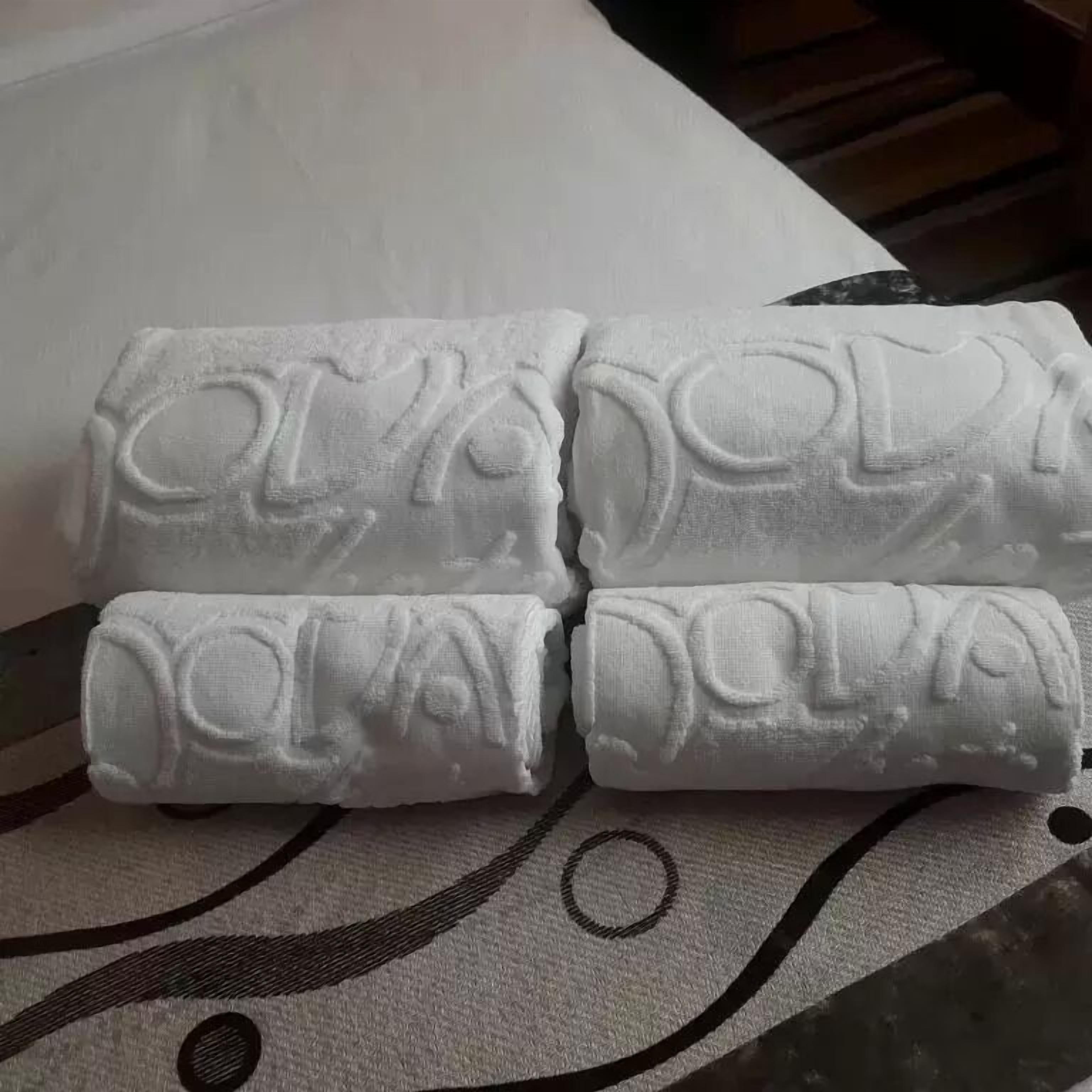 Cuatro toallas enrolladas con texto en relieve, sobre un tejido estampado.