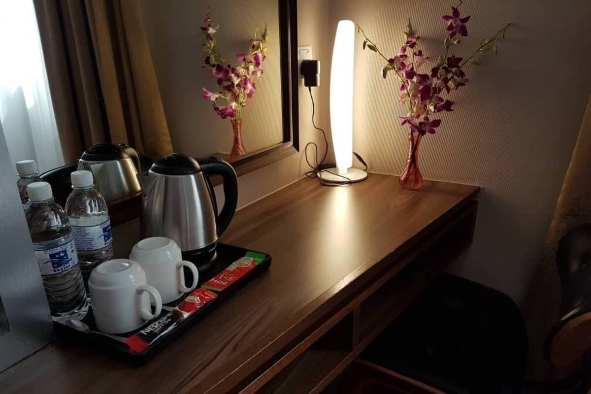 A hotel room with a wooden desk, a kettle, two cups, a tray with water bottles and a box of Nespresso coffee pods, and two vases with flowers.