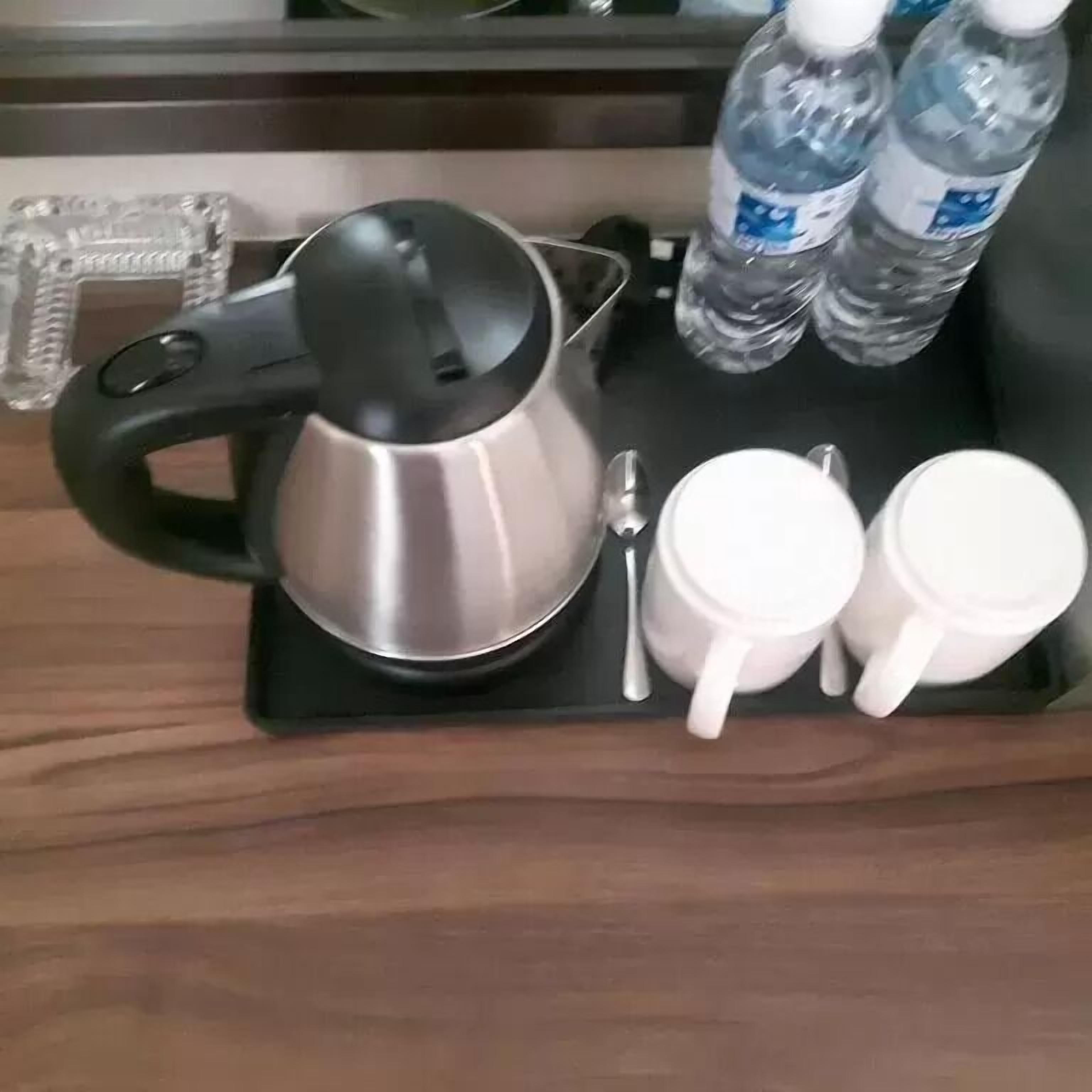 A tray with a stainless steel electric kettle, two white mugs, a spoon, and two bottles of water.