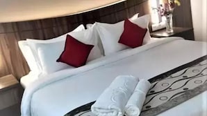 A neatly made bed with white and red pillows, a rolled white towel, and a decorative black and white headboard. - Nova Hotel Miri (Miri)