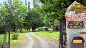 Schild für das Schloss Château de Bremesnil, ein befahrbarer Eingang mit einem Feldweg, der durch ein bewaldetes Gebiet führt.