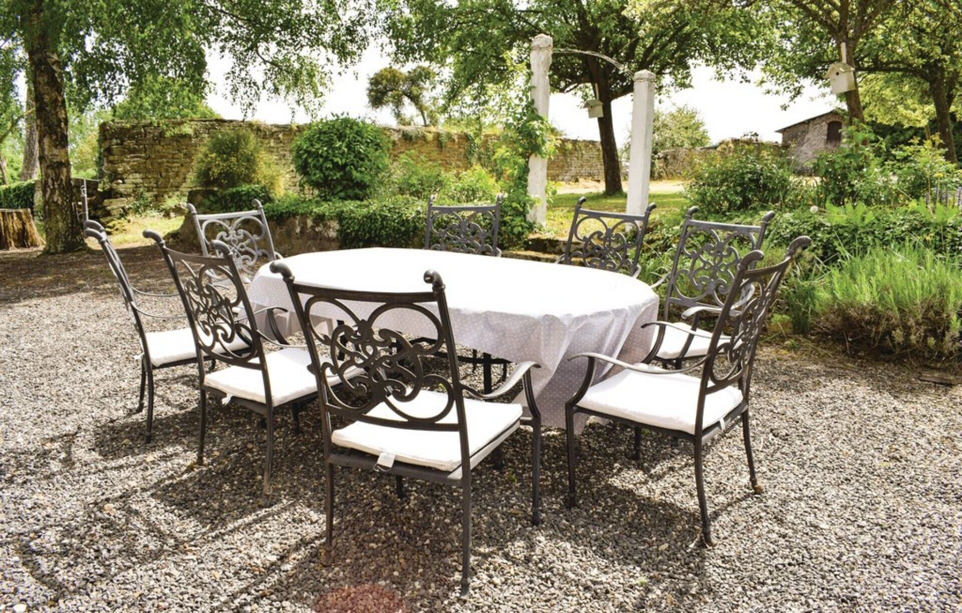 Un área de comedor al aire libre con una mesa redonda y seis sillas, rodeada de grava y follaje.
