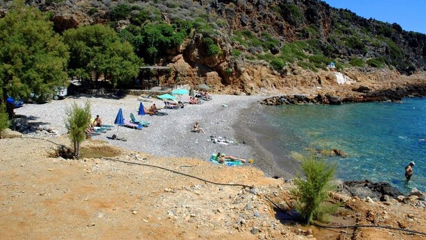 A beach with rocky terrain, clear water, and a few umbrellas. - Ravdoucha-Kissamos for rent  Country house (Ravdoucha)