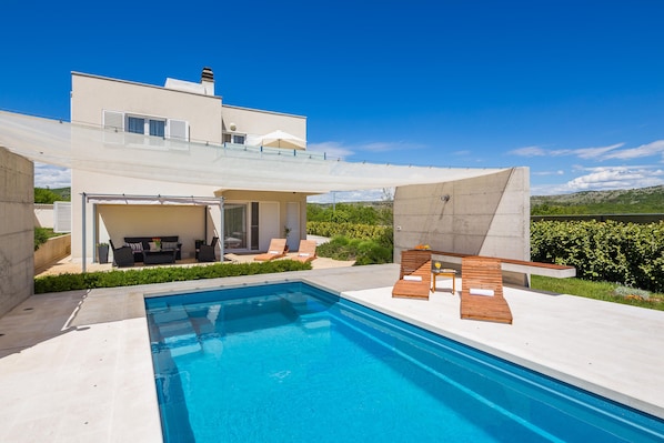 Une maison moderne dotée d’une piscine, d’un espace salon extérieur et offrant une vue sur les collines.