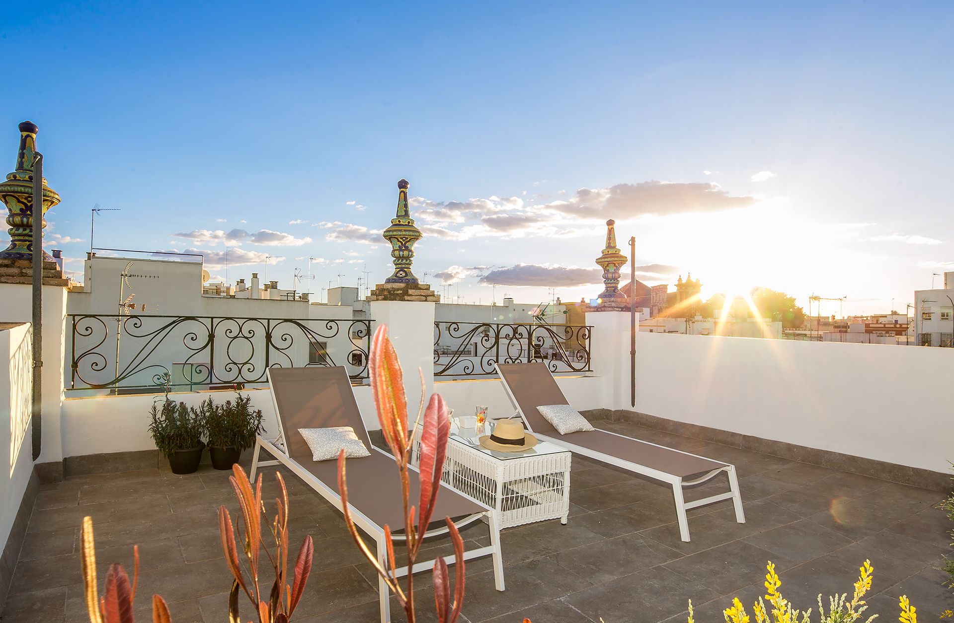 A rooftop terrace with two sun loungers, a small table, and potted plants.