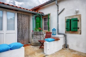 Un petit espace extérieur clos, avec un mur blanc, un toit recouvert de tuiles rouges, une porte verte et une lanterne bleue.