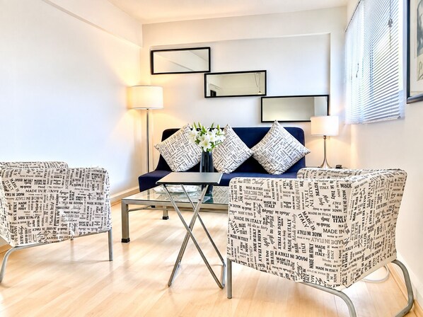 Una sala de estar moderna con una mesa de centro de vidrio, dos sillones estampados, un sofá con almohadones decorativos y espejos montados en la pared.