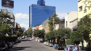Una strada cittadina con un alto edificio blu, auto parcheggiate e alberi lungo il marciapiede.