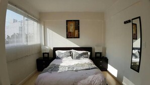 Camera da letto con un letto grande, due comodini, una finestra con persiane e uno specchio fissato alla parete.
