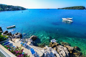 Vista costera con aguas azul turquesa, barcos y un litoral rocoso con sillones de playa.