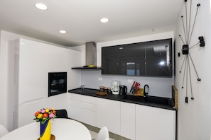 Una cocina moderna con armarios blancos, encimera negra y horno empotrado. Hay una mesa de comedor con un florero.