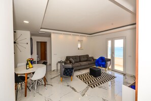 Una sala de estar moderna con un sofá, una mesa de comedor con sillas, un jarrón decorativo y vistas al exterior a través de un ventanal.