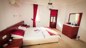A bedroom with a bed, a dresser, a mirror, and a window with red curtains.