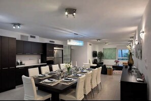 Eine moderne Küche mit dunklen Schränken, eine Essecke mit einem großen Tisch für sechs Personen und ein Wohnbereich mit einer Couch und einem Fernseher.