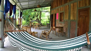 A hammock in a covered outdoor area with wooden furniture and a brick wall. - Real family hostel, Hospedaje La Penita, 2 person room  (Altagracia)