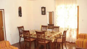 Un comedor con una mesa redonda, seis sillas de madera, un mantel con estampado floral, un reloj en la pared y una ventana con cortinas.