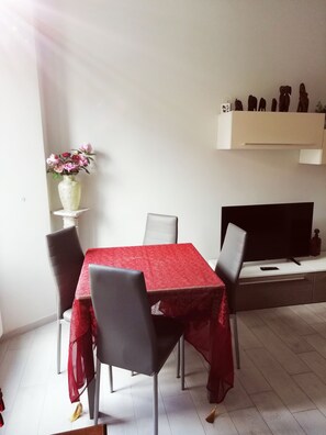 Ein Essbereich mit rotem Tischlein, vier Stühlen, einer Blumenvase und einem Fernseher auf einem Schrank.