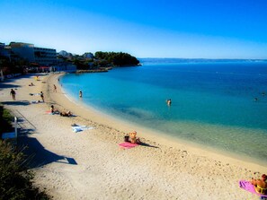 Ein Strand mit klarem, blauem Wasser, Menschen, die sich sonnen, und Gebäuden im Hintergrund.