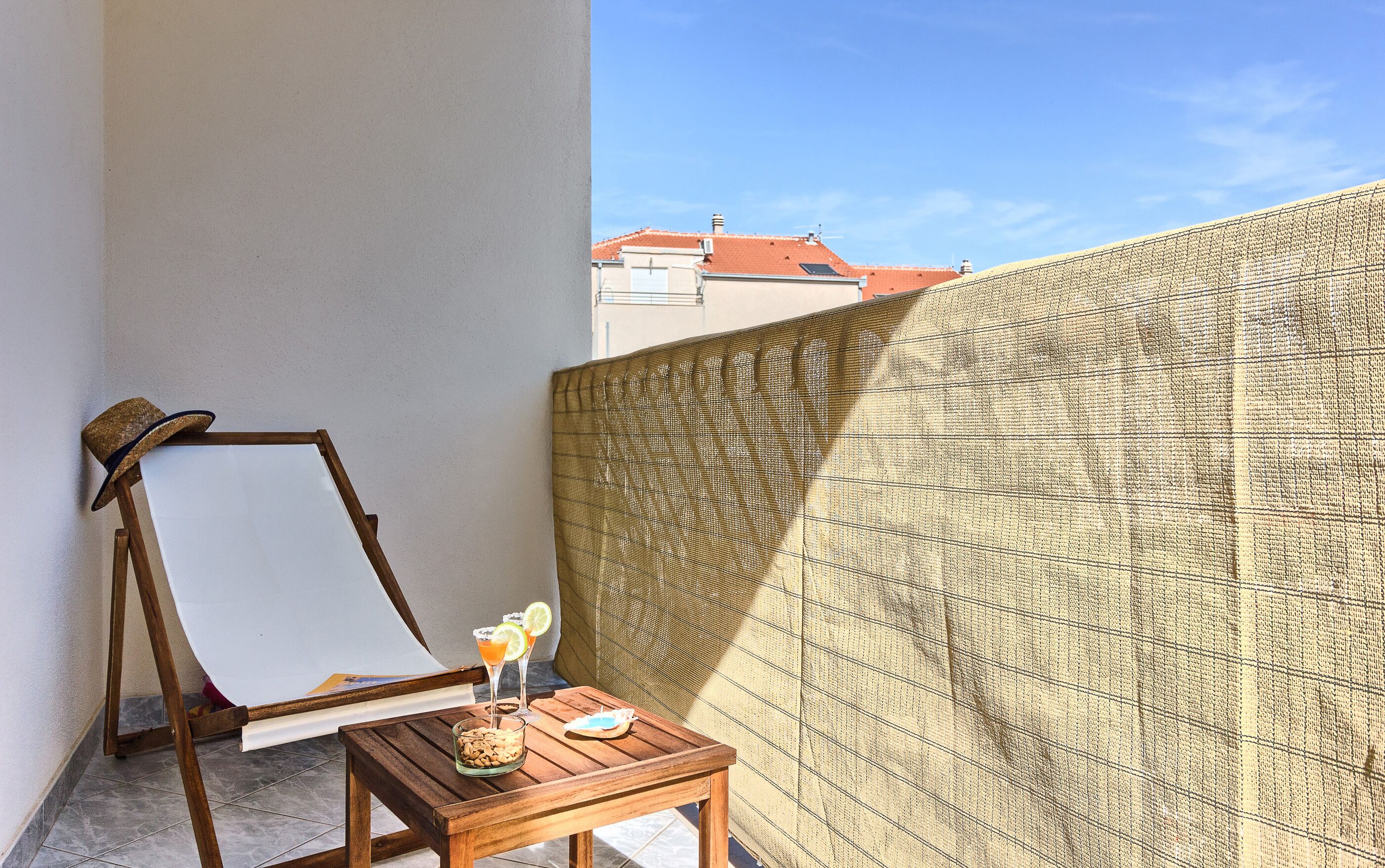 A wooden easel with a blank canvas, a small wooden table with a glass of drink and snacks, and a patterned wall.