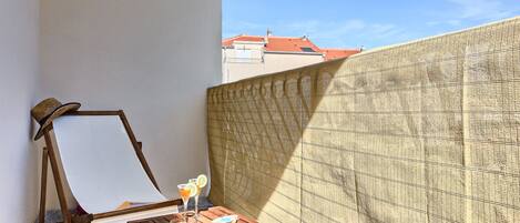 A wooden easel with a blank canvas, a small wooden table with a glass of drink and snacks, and a patterned wall.