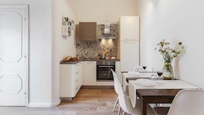 Una cocina compacta con armarios blancos, horno empotrado y un comedor con mesa para dos.