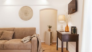 Una sala de estar moderna con un sofá color beige, una mesita de noche con una lámpara, un televisor montado en la pared y un adorno mural.