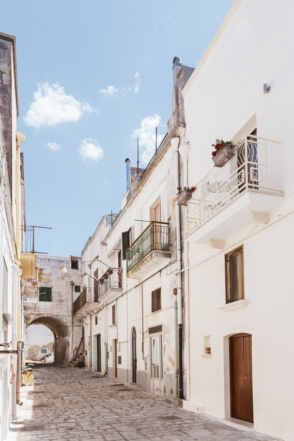A narrow cobblestone street flanked by historic buildings with balconies and a stone archway.