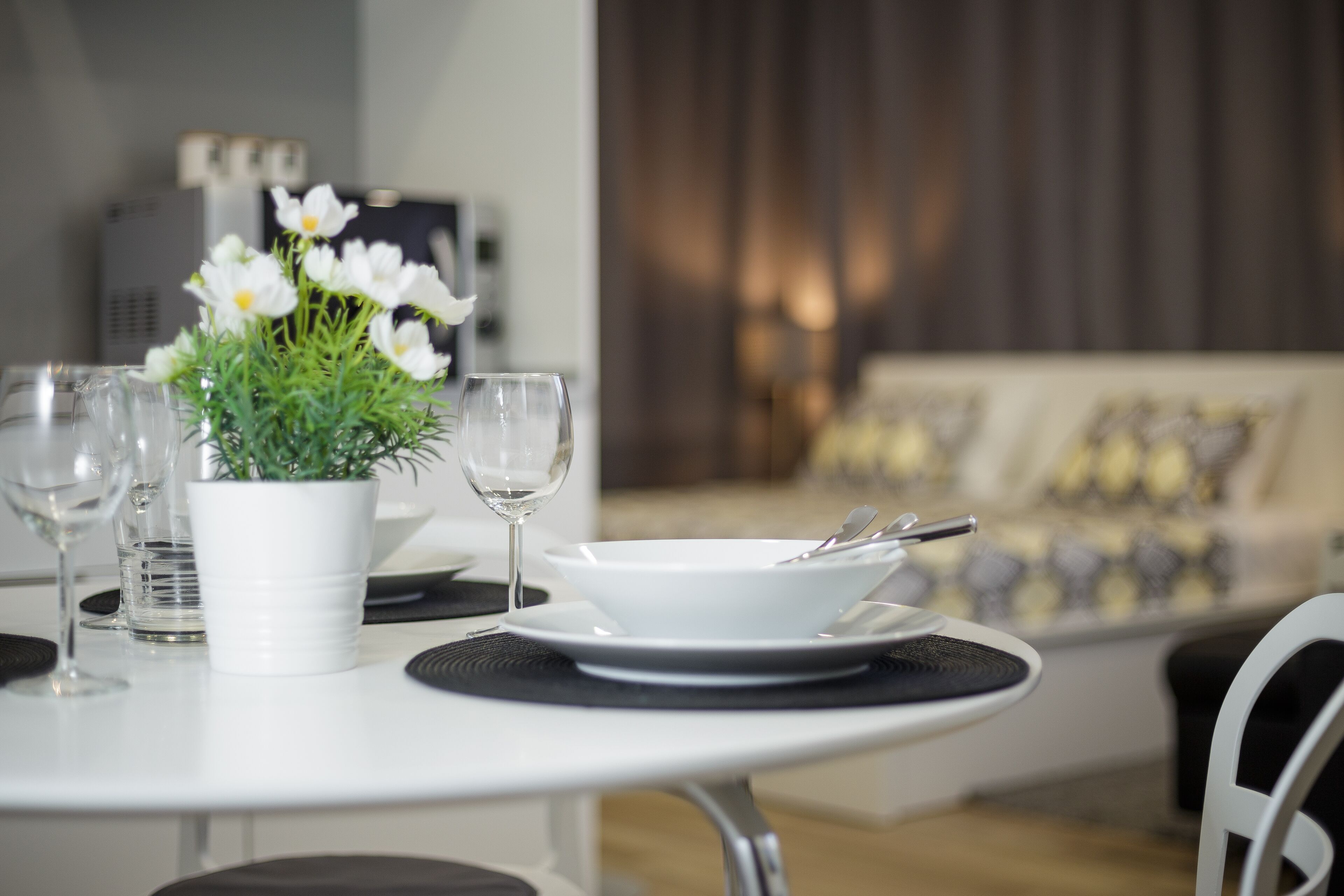 Une table à manger dressée avec de l’assiette, des bols et des couverts blancs, un vase blanc rempli de fleurs et des verres à vin.