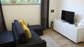 Uma sala de estar moderna com um sofá seccional, uma TV de tela plana sobre um armário branco e um banquinho.
