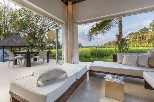 A bedroom with a large window, a bed, a sofa, and a dining area with a table and chairs.