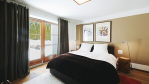 A bedroom with a large bed, a sliding glass door to a balcony, and two framed pictures on the wall.