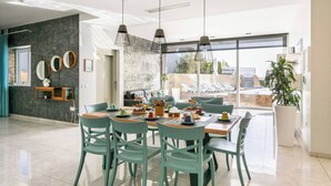 A modern dining area with a large table, multiple chairs, and hanging pendant lights. - Villa Dorado with Pool, Sauna, Jacuzzi, Gym & more (Marsaskala)