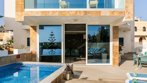 A modern two-story house with a swimming pool, outdoor seating, and a glass balcony. - Villa Dorado with Pool, Sauna, Jacuzzi, Gym & more (Marsaskala)