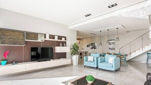 A modern living room with a flat-screen TV, a coffee table with a plant, and a staircase leading to an upper level. - Villa Dorado with Pool, Sauna, Jacuzzi, Gym & more (Marsaskala)
