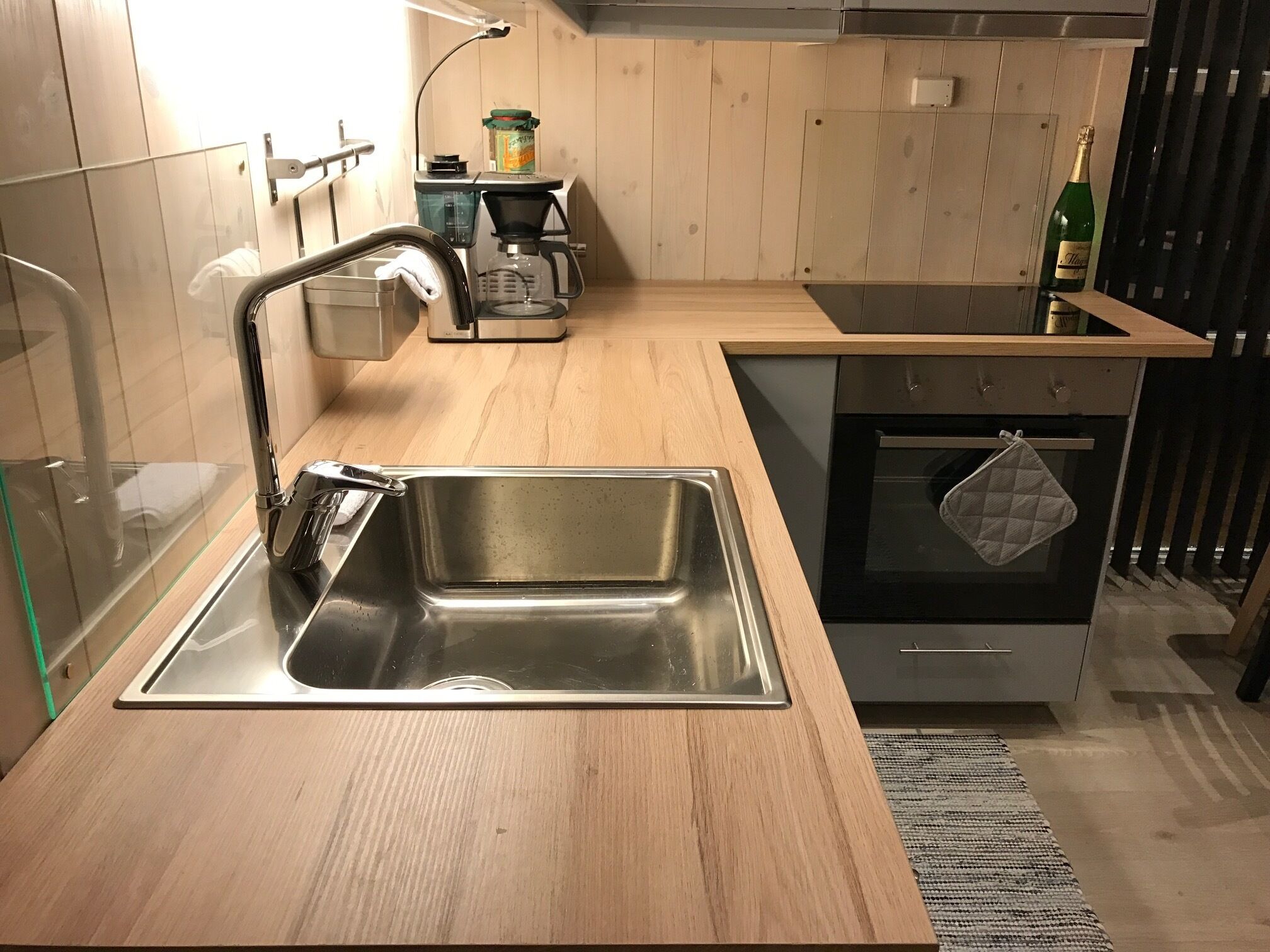 A modern kitchen with a stainless steel sink, wooden countertops, a built-in oven, and a coffee maker.