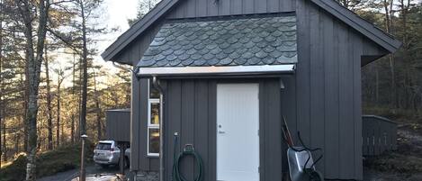 A small, single-story wooden shed with a white door, a metal roof, and a small window.