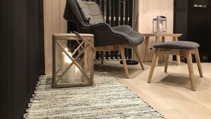 A cozy seating area with a cushioned chair and ottoman, a small table, and a glass lantern on a woven rug. - Fam friendly furniture cottage in a quiet environment. 8 Pers Sauna and Jacuzzi (Stord)