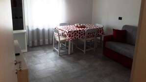Ein kleiner Essbereich mit Tisch, der mit einer rot-weißen Tischdecke bedeckt ist, zwei Stühlen und einer Uhr an der Wand.