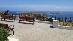 Eine gepflasterte Terrasse mit Bänken mit Blick auf eine Küstenlandschaft.
