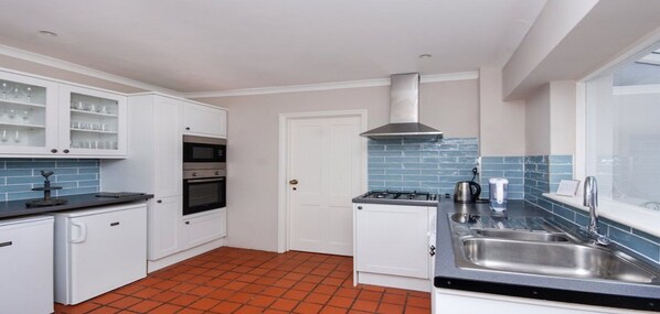 A compact kitchen with white cabinets, a black countertop, a stove, a microwave, and a sink. - Grebe Cottage Bonchurch Isle of Wight . Idyllic setting. (Ventnor)