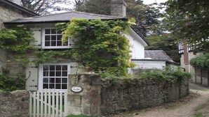 A stone cottage with a white door and window, surrounded by a stone wall and covered in ivy. - Grebe Cottage Bonchurch Isle of Wight . Idyllic setting. (Ventnor)