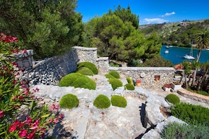 A stone pathway with green topiary, a stone wall, and a view of a harbor with boats. - Beautiful Dalmatian style villa with magnificent garden (Bobovisca na moru/Bobovisca at sea/)