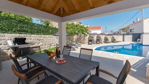 Un espacio al aire libre techado con piscina, muros de piedra y una parrilla.