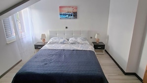 Un dormitorio con techo inclinado, una cama con cubierta acolchada, dos mesitas de noche con lámparas y un cuadro colgado en la pared.