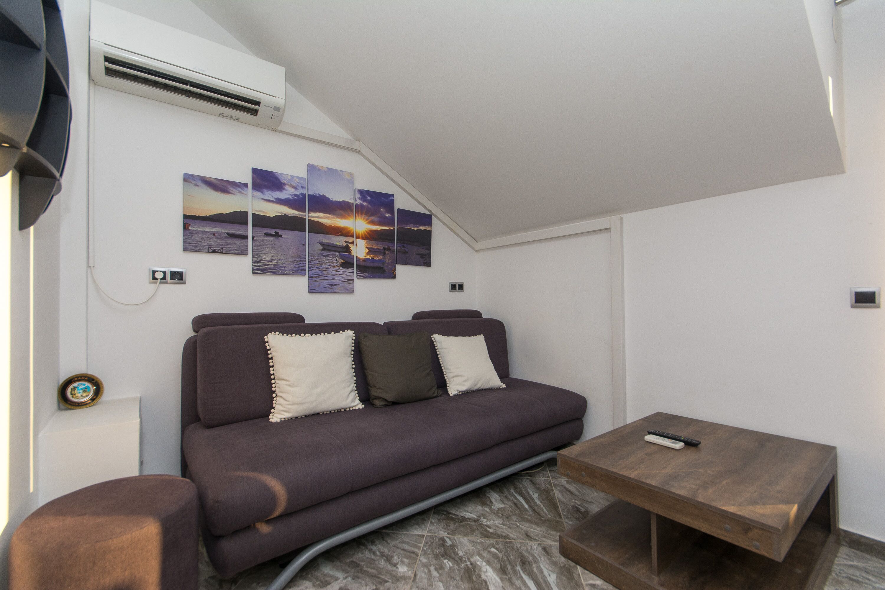A modern living room with a sofa, a coffee table, and wall art depicting a sunset over water.